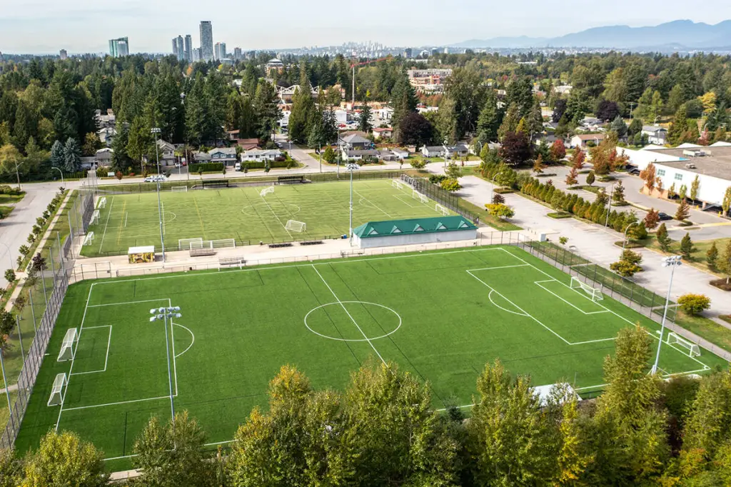 Aerial view of the turf pitches at South Surrey Athletic Park, with floodlights and the Vancouver skyline in the distance